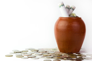 Banknotes are rolled into pot or jar is a kind of pottery and coins are stacked on the white...