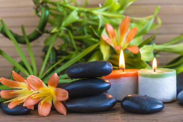 Fototapeta na wymiar Spa concept with massage stones, orange flowers, green bamboo stems and burning candles