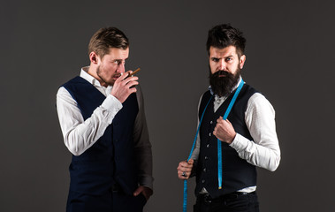 Tailor on strict face ready to take measurements, grey background.