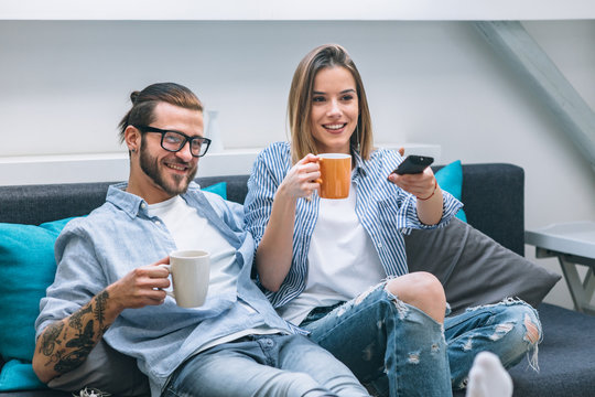 Young couple sitting on the couch, drinking coffee and watching tv