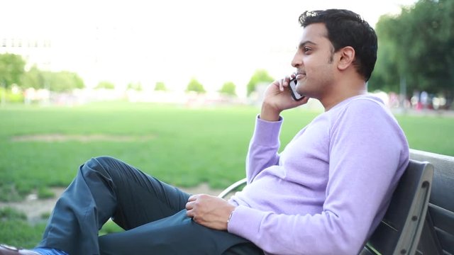 Closeup portrait, handsome young business man, happy guy in purple sweater, using cell phone, smiling, having pleasant conversation, isolated outside background. Human emotions, expression