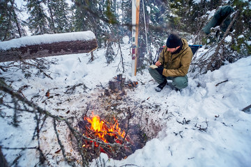 Summary of the day. Thoughtful man in military clothes with a notebook in his hand at campfire in winter in the tundra forest.