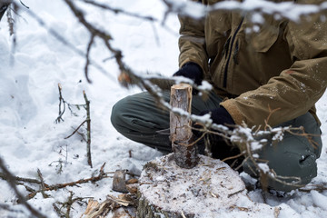 Cutting wood into smaller pieces with knife for bonfire in the winter in tundra forest.