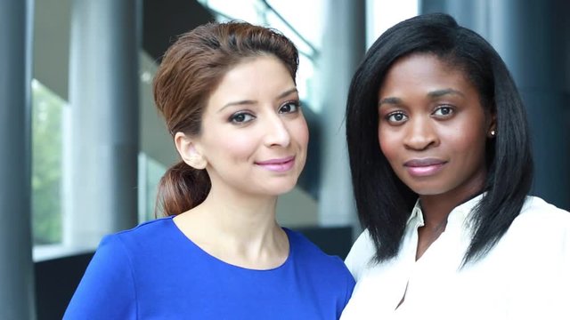 Closeup portrait of two confident workforce women, isolated indoor office background