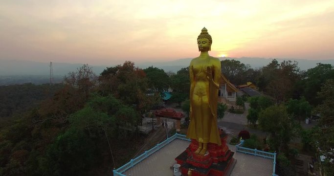 aerial photography sunset above golden buddha standing statue at wat Phra That Jom Wae Chiang Rai