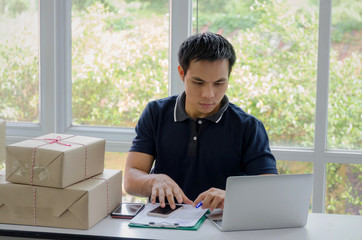 Start up. young man happy after new order from customer with laptop computer, mobile phone, delivery packaging box on table, small business owner working at home office, SME, shopping online concept