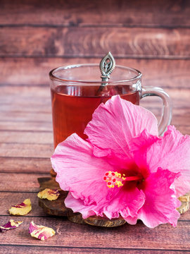 Glass Cup with red tea pink hibiscus flower on dark wood background