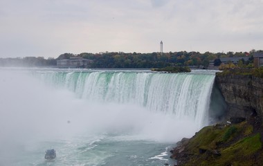 Fototapeta premium Beautiful and impressive panorama of the Niagara Falls in Ontario (Canada) on a bright colorful (red, orange, yellow) autumn day with water crashing down the falls onto rocks creating lots of mist