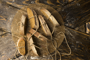 Conceptual still life photography of pieces of bread tied with twine, lying on an ancient wooden table made of rough boards on a round grid.