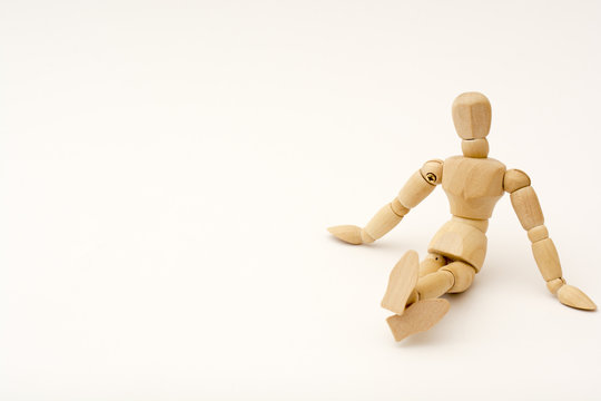 A wooden person sits on the floor, his legs are crossed, head looks at the viewer