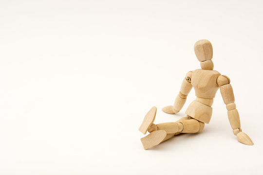 A wooden person sits on the floor, his legs are crossed, head looks at the viewer and slightly tilted to the right