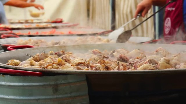 Preparation of paella in large frying pans standing in a row.