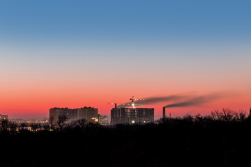 Cityscape with dramatic sky  sunset. Silhouette of buildings and smoking pipes. Urban industrial city.  Environmental pollution