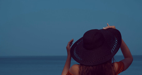 Back view of girl's head with hat relaxing in the sun during summer holiday on the tropical beach over sea and sky background