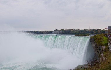 Fototapeta premium Beautiful and impressive panorama of the Niagara Falls in Ontario (Canada) on a bright colorful (red, orange, yellow) autumn day with water crashing down the falls onto rocks creating lots of mist