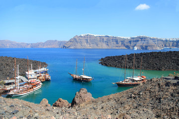 Fototapeta premium Tourist excursion boats at small port on volcano of Santorini