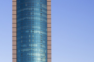 Obraz premium A multi-storey brick building under construction, against a blue sky background. High multi-story building. Skyscraper. Blue windows. Mirror