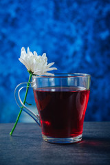 A cup of tea with mint on a dark table, next to a white flower
