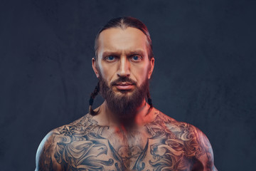 Fototapeta premium Close-up portrait of a muscular bearded tattoed male with a stylish haircut, isolated on a dark background.