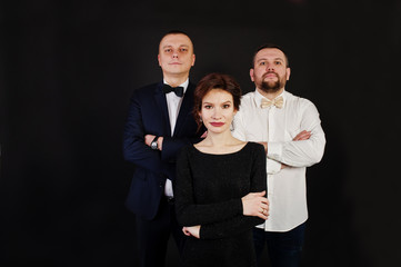 Elegance woman in black evening dress with two man in suit posed on studio isolated on black. Trio band.