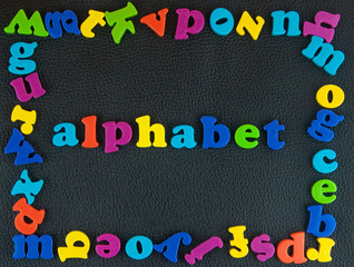 Alphabet written word.Frame of plastic alphabetical letters on the black leather background.