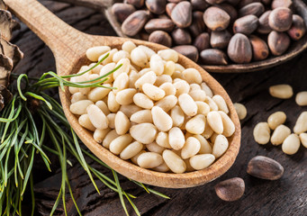 Pine nuts in the spoon and pine nut cone on the wooden table. Organic food.