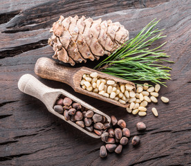 Pine nuts in the wooden scoops and pine nut cone on wooden background. Organic food.