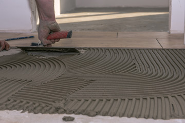 A tiler prepares the floor for laying tiles with tile adhesive. Concept: craft or construction site