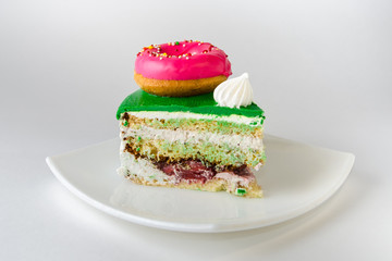 Piece of white cake with green chocolate icing on top, decorated with pink and yellow donuts and a bright meringue.