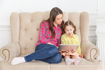 Mother and daughter on sofa at home and playing with pc tablet together