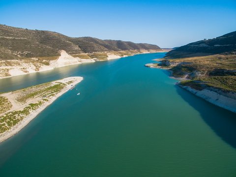 Aerial Bird's eye view of artificial lake at the largest dam in Cyprus, Kouris reservoir, Limassol. View of the river split peninsula, earthfill embankment and hills around water from above.