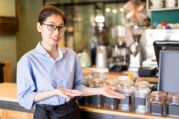 Fototapeta na wymiar Cheerful barista showing coffee varieties and offering to buy tasty coffee. Positive young Asian restaurant manager presenting coffee. Drink establishment concept