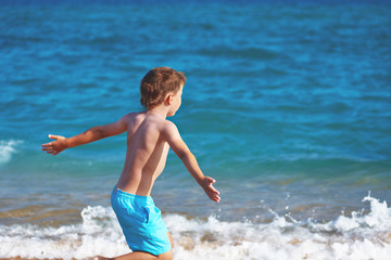 European boy is running along the seashore. His arms are opend to the sides.