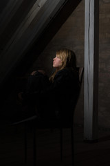 trauriges Teenager M&auml;dchen auf einem Stuhl im Dunkeln sitzend und zum Fenster guckend