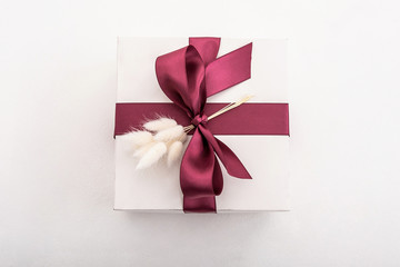 white box with a burgundy color ribbon and flowers on a white background