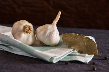 On the green napkin on black style table, seasonings: garlic, black pepper peas and bay leaf