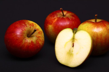 Three red whole apples and one sliced in half isolated on a black background