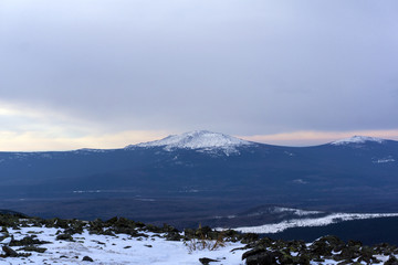 winter wooded mountains with a snow peak or a volcano cone in the distance
