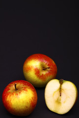 Fototapeta na wymiar Two whole red apples and one sliced in half isolated on a black background