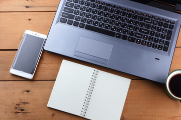 Laptop and cup of coffee on a wooden background, workstation on an old desk, smartphone and a notebook, pen and glasses in the workplace, designer workstation, office