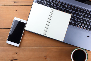 Laptop and cup of coffee on a wooden background, workstation on an old desk, smartphone and a notebook, pen and glasses in the workplace, designer workstation, office