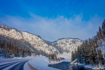 Outdoor view of winter road covered with heavy snow and ice in the forest and small river at one...