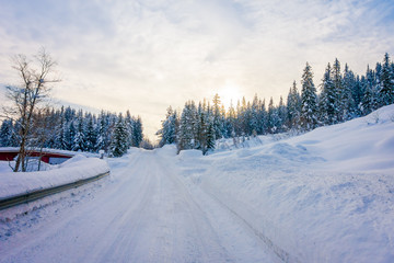 Fototapeta na wymiar Outdoor view of winter road covered with heavy snow and ice in the forest and a gorgeous sunset view