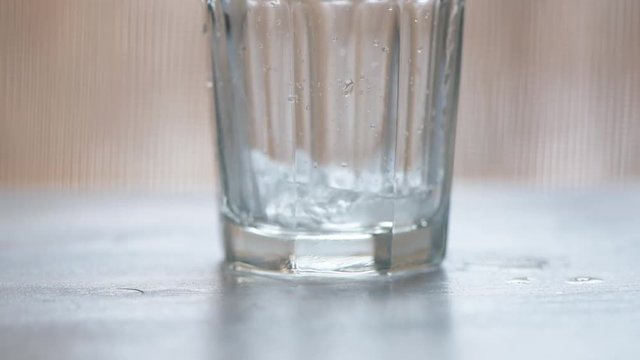 Pouring fresh cold fizzy water into drinking glass on the table, ungraded flat style footage