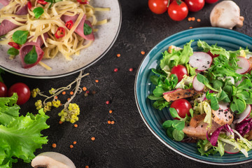 Delicious dinner. Italian pasta and fresh vegetable salad on the black background. Healthy food. Close up. Top view