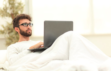 handsome man working on laptop lying on bed