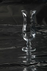 Still life with one single modern transparent and fragile (cocktail) glass on a table with a black background