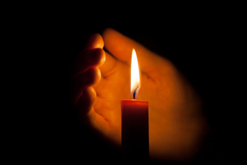 A burning candle at night. Symbol of life, love and light, protection and warmth. Candle flame glowing on a dark background.