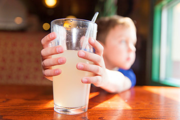child holding a glass with lemonade. the boy reaches for a glass of juice and looks out the window....