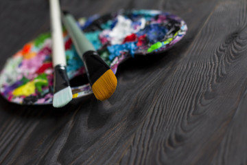 Brushes and art palette with paint on brown wooden background